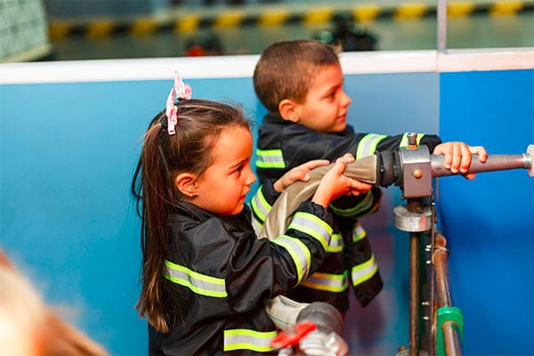 Preschool boy and girl wearing firefighter attire with firefighting hose on a demo at a Preschool & Daycare Serving Hesperia, CA