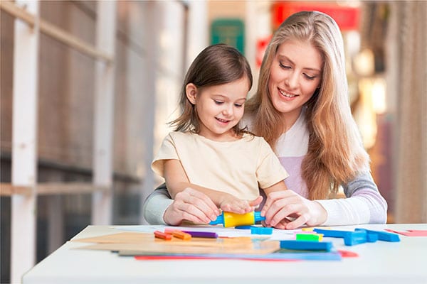 Beautiful teacher helping a cute little preschool girl molding a colored clay with plastic molding pin at a Preschool & Daycare Serving Hesperia, CA