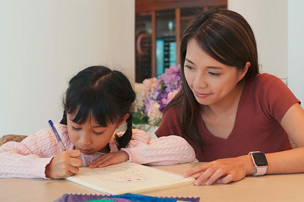 Beautiful teacher watching a young little preschool girl drawing on a paper at a Preschool & Daycare Serving Hesperia, CA