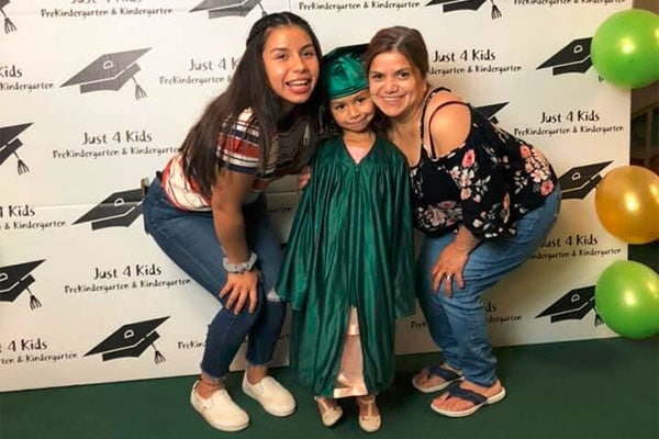 Happy teacher with mother and daughter wearing graduation toga at a Preschool & Daycare Serving Hesperia, CA