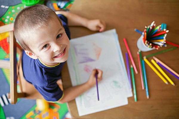 Happy young little kid boy while coloring and drawing on a paper with color pencils on the table at a Preschool & Daycare Serving Hesperia, CA