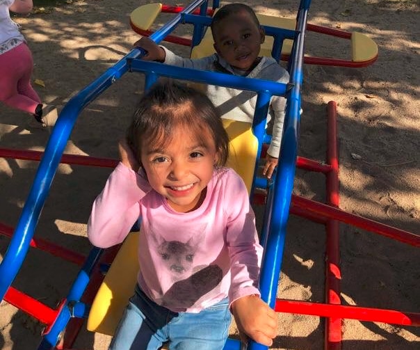 Happy cute little preschool girl wearing pink sweatshirt playing on monkey bars at the playground at a Preschool & Daycare Serving Hesperia, CA