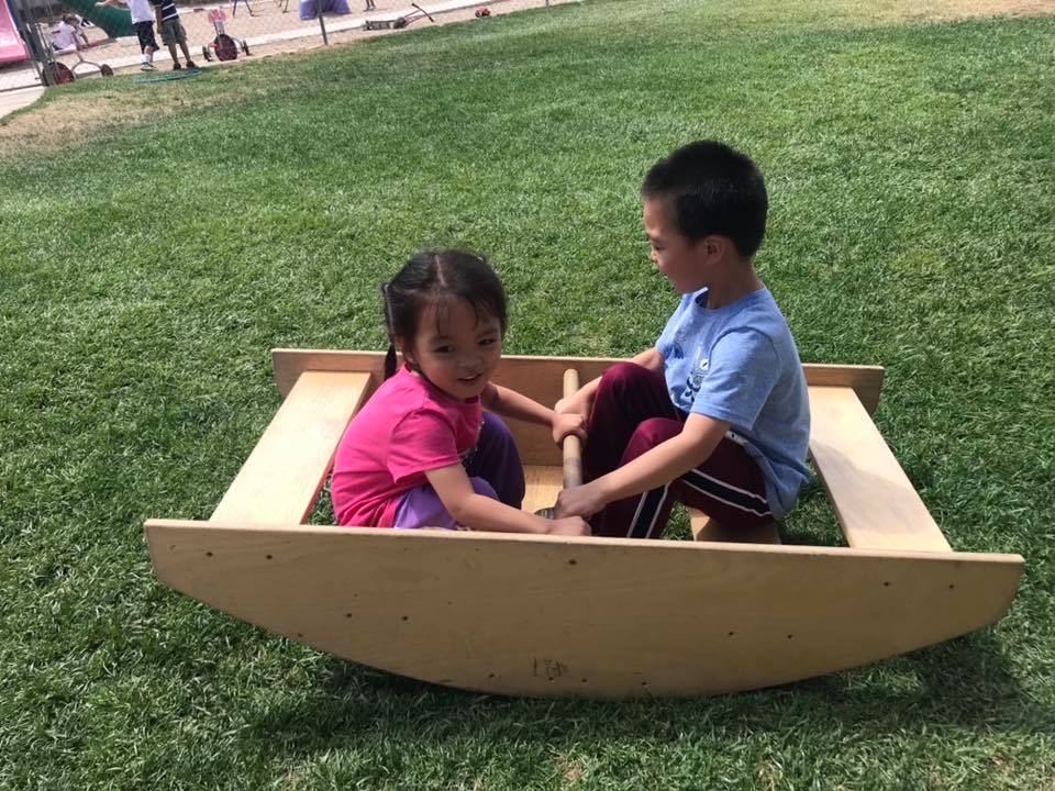 Two little preschool kids on a wooden DIY seesaw on the playground at a Preschool & Daycare Serving Hesperia, CA at a Preschool & Daycare Serving Hesperia, CA