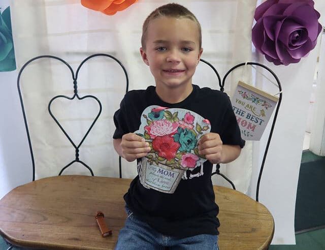 A kid boy holding a colorful flower designed artwork for mom at a Preschool & Daycare Serving Hesperia, CA