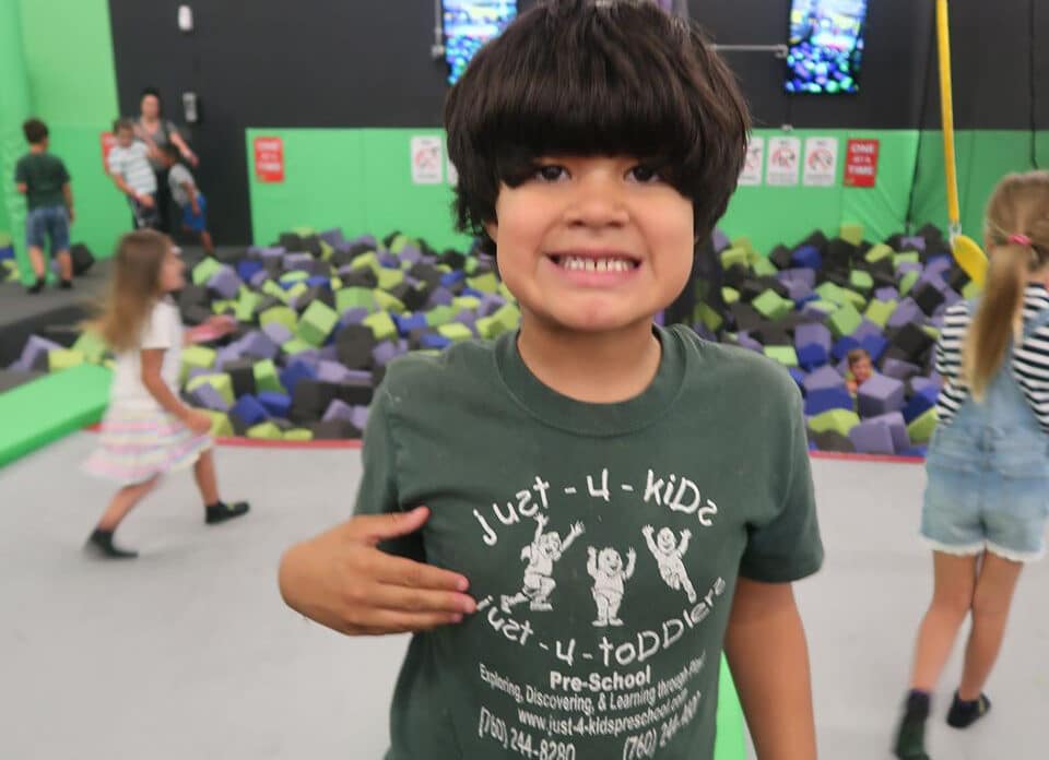 Smiling preschool kid wearing just-4-kids school shirt at an indoor play center at a Preschool & Daycare Serving Hesperia, CA