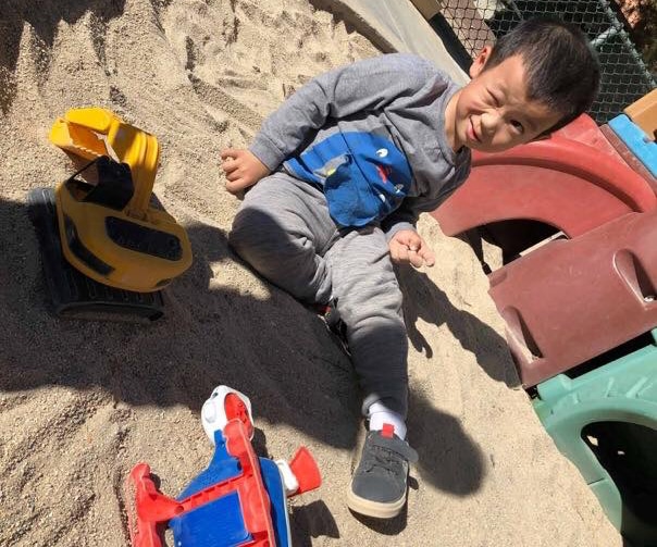 Winking preschool kid boy playing on the sand at a playground at a Preschool & Daycare Serving Hesperia, CA