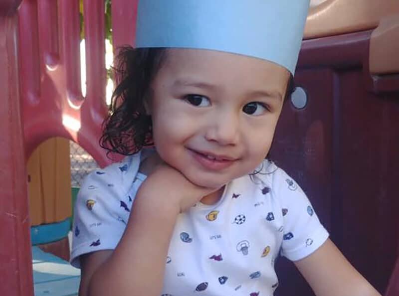 Cute preschool little girl smiling wearing a blue paper graduation hat while in the playground at a Preschool & Daycare Serving Hesperia, CA