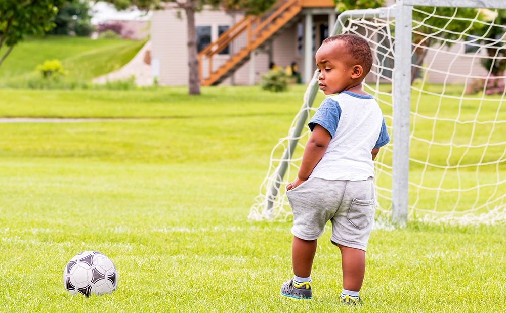 African american preschool boy looking at the soccer ball while in the field next to the soccer goal at a Preschool & Daycare Serving Hesperia, CA