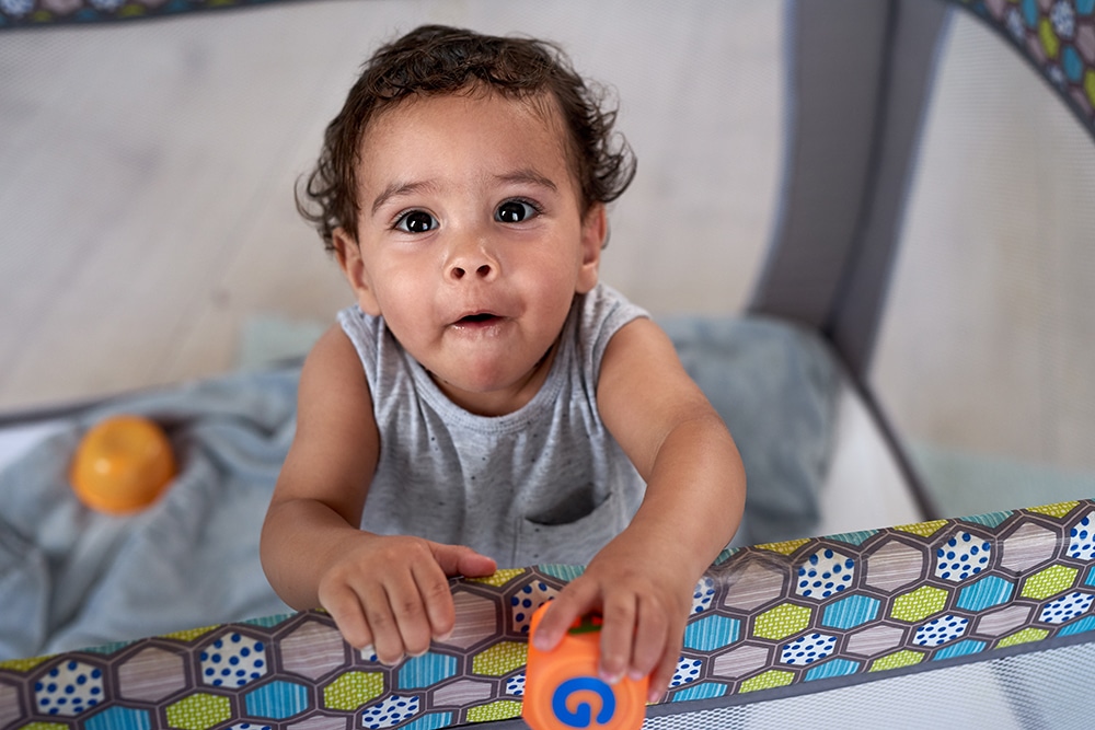 Portrait of cute baby boy in cot holding a toy block, childhood development educational at a Preschool & Daycare Serving Hesperia, CA
