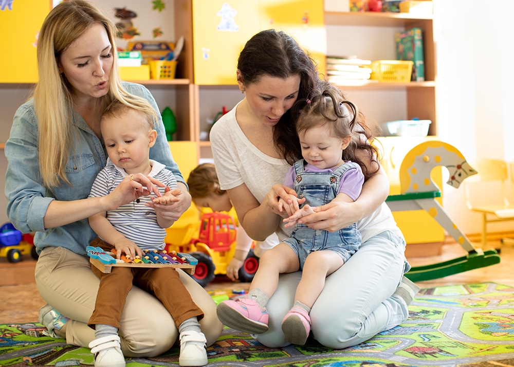 Babies toddlers playing with colorful educational toys together with mothers in children nursery playroom at a Preschool & Daycare Serving Hesperia, CA