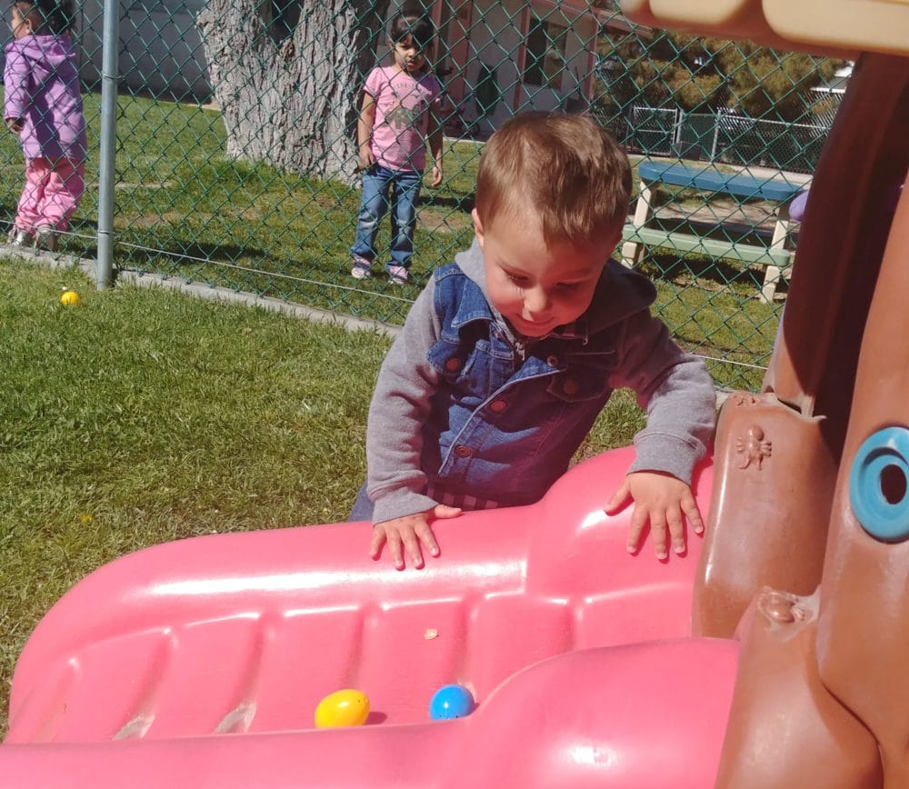 Toddler boy trying to climb a pink slide at the playground being watched by another young little girl wearing pink at a Preschool & Daycare Serving Hesperia, CA