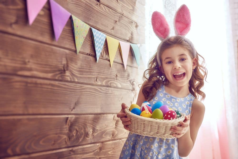 Cute young little girl wearing rabbit ears holding a basket full of colorful painted eggs at a Preschool & Daycare Serving Hesperia, CA