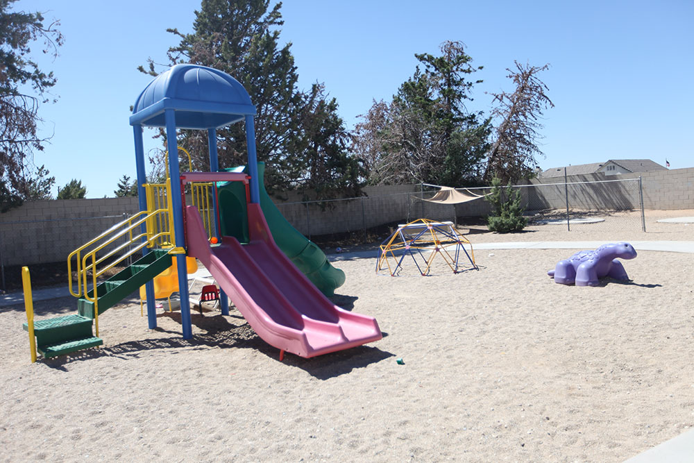 sandy playground with a colorful slide and a geo-dome climber jungle gym, violet dino-ride at a Preschool & Daycare Serving Hesperia, CA