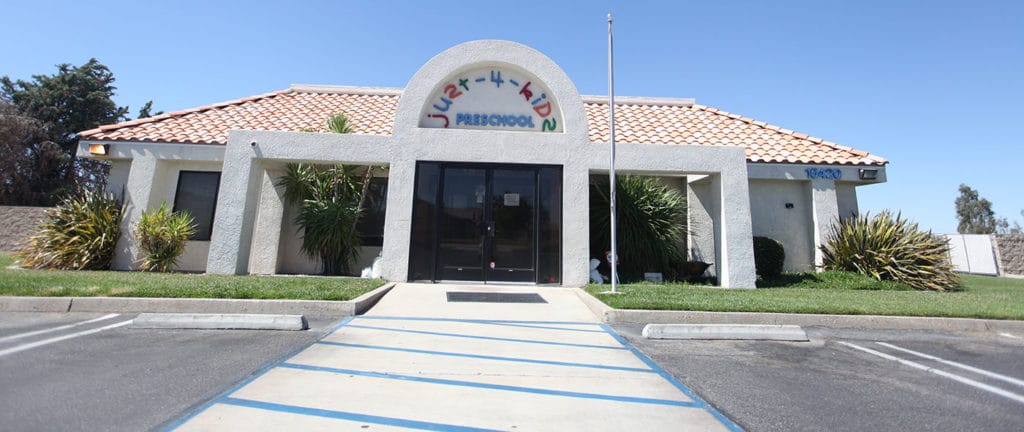 Just-4- kids Preschool office outside front view with flag pole, glass door, and parking spaces at a Preschool & Daycare Serving Hesperia, CA